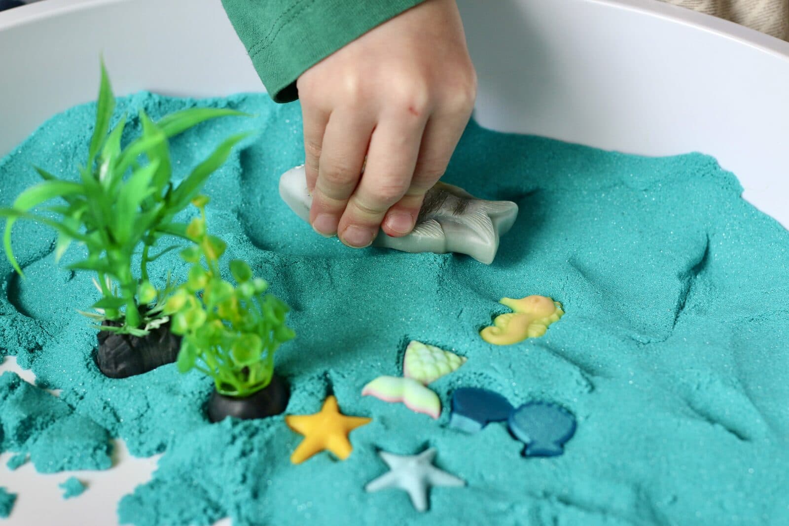 Kind speelt met oceaan sensorische tray met turquoise zand